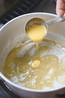 鍋の中に沸騰した透明がかった液体が入っており、その上にスプーンに入った淡い黄色の液体を垂らしている調理中の様子を写した写真