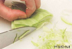 左手でしっかりと押さえたキャベツを、包丁を使って端から一定の幅で細かく千切りにしている様子の写真