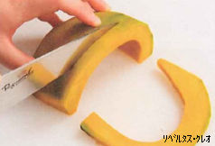 種とわたを除いた薄切りのカボチャを左手で固定し、右手の包丁で皮の面から実の面に向かって一定の幅のくし型に切り分けている様子を捉えた写真