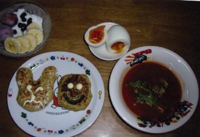 左上から時計回りにバナナやブルーベリーを添えたヨーグルト、半分に切られた半熟のゆで卵、トマトベースのスープボウル、白い皿にうさぎと顔の形のおやきが置かれている写真