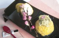 上にとろろ昆布があしらわれ桃の花枝が添えられた、黄色くて丸いエビれんこんまんじゅうの写真