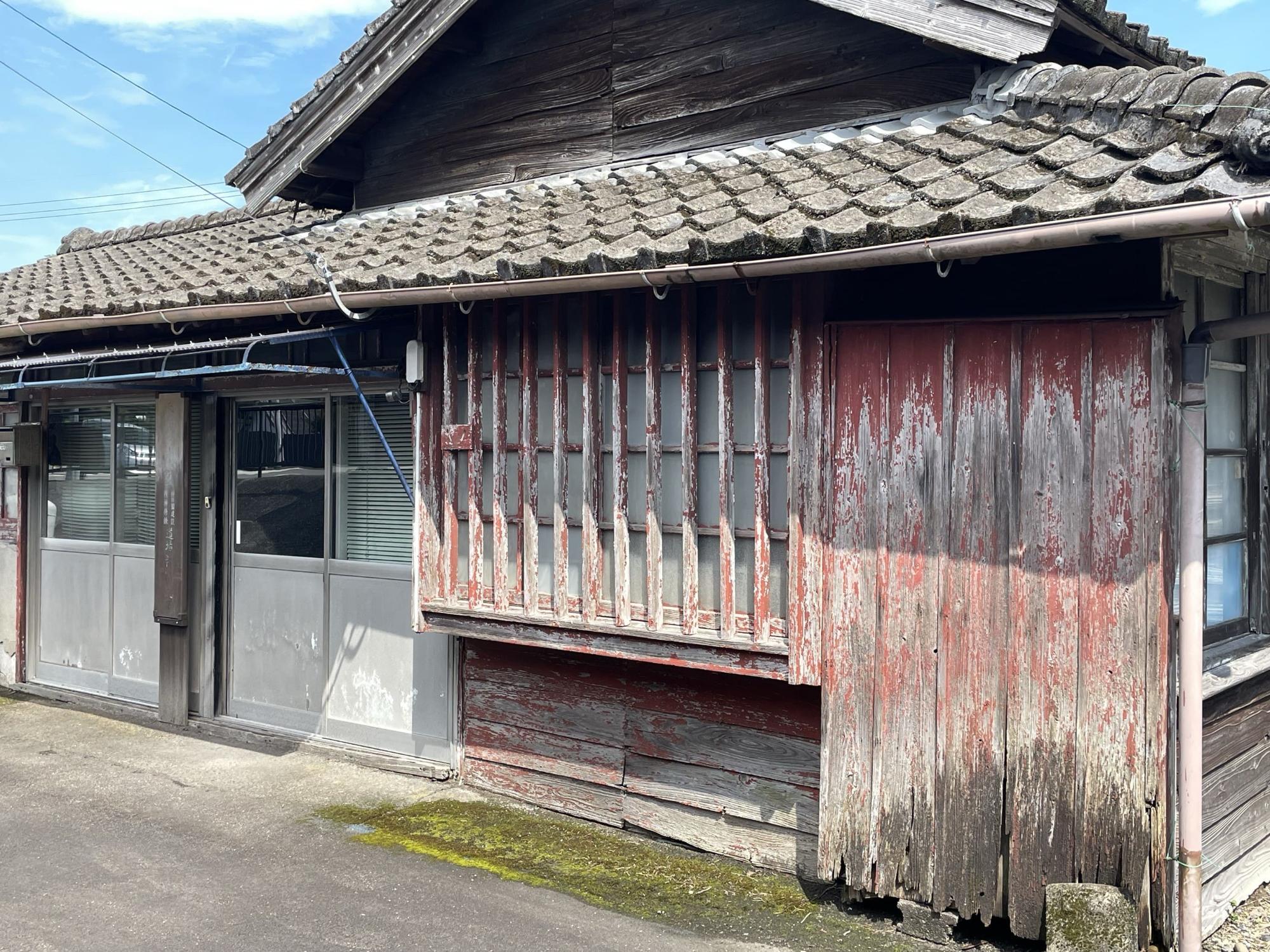 瓦屋根と木造の壁の古い平屋の建物で、格子状の窓枠、銀色のアルミサッシの引き戸になっている平屋建ての物件の写真