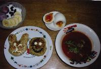 左上から時計回りにバナナやブルーベリーを添えたヨーグルト、半分に切られた半熟のゆで卵、トマトベースのスープボウル、白い皿にうさぎと顔の形のおやきが置かれている写真