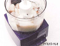 四角い土台を持つ家庭用フードプロセッサー本体の透明な容器の中に、殻を剥いた複数の生のむきえびが入れられ、調理を開始する直前の状態を斜め上から捉えた写真