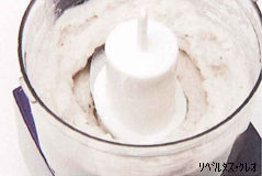 濃い紫色の土台を持つフードプロセッサーの透明な容器の中で、生のむきえびが攪拌され、粘り気のあるなめらかな白色のミンチ状に変化した状態を真上から捉えた写真