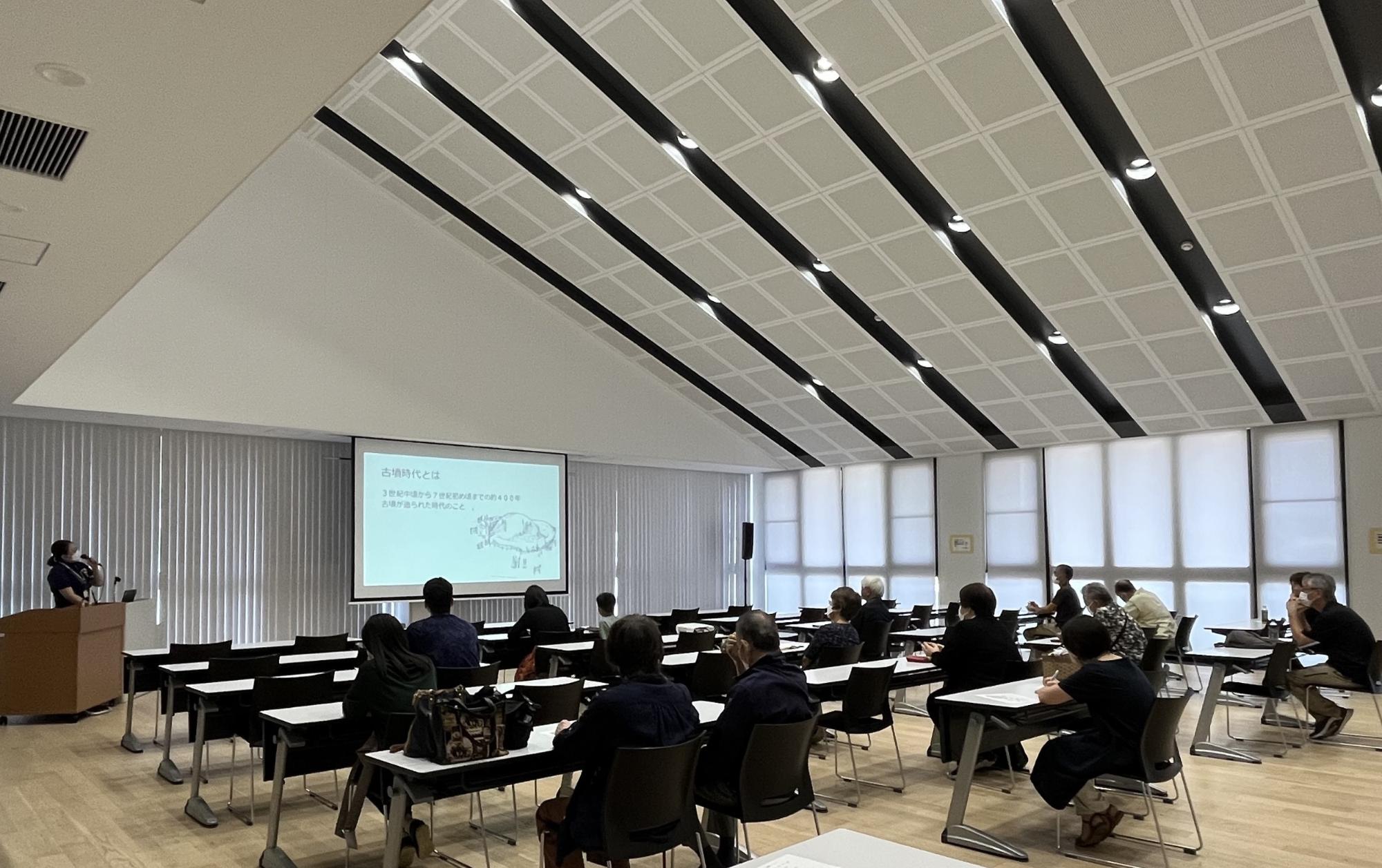 解放感のある会議室で、前方のスクリーンには資料が映しだされ、参加者の方々が長机の席に座って熱心に話を聞いている講座の様子の写真