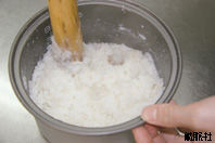 炊飯器で炊きあがった米と大和芋を木でつぶしている写真