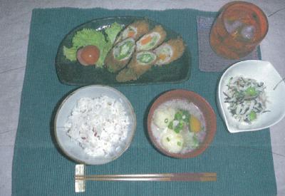 緑色のランチョンマットの上に断面の彩りが綺麗な肉巻きフライの主菜の下に雑穀ごはん、具沢山の汁物、横にサラダが並べられた写真