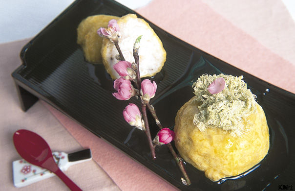 上にとろろ昆布があしらわれ桃の花枝が添えられた、黄色くて丸いエビれんこんまんじゅうの写真