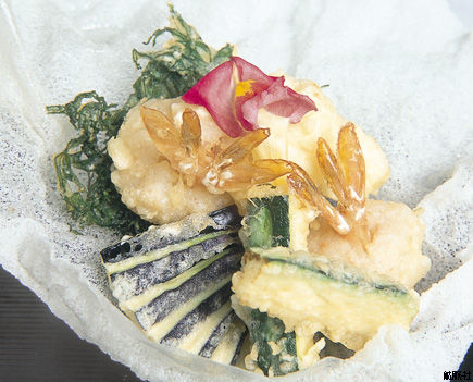 海藻や野菜と共に彩りよく配置され、上に花びらが添えられた天ぷらの写真