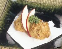 白い紙の上に盛り付けられ、薄切りのリンゴとパセリが添えられた鶏のから揚げの写真