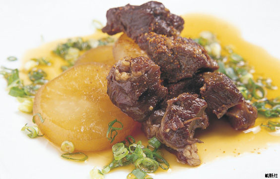 刻んだ青ねぎが散らされ飴色に深く煮込まれた大根と柔らかそうな牛すじの煮込みの写真