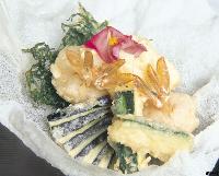 海藻や野菜と共に彩りよく配置され、上に花びらが添えられた天ぷらの写真