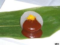 笹の葉の上に載せられた白い円形の大根にたっぷりと赤味噌がかけられ、細長く刻まれた黄色い柚子の皮が美しく添えられている、大根の味噌かけ柚子和えの写真