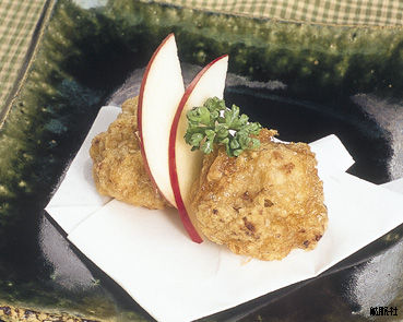 白い紙の上に盛り付けられ、薄切りのリンゴとパセリが添えられた鶏のから揚げの写真