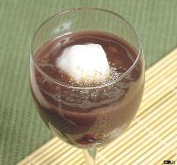 透明なワイングラスの中に、ぜんざいが満たされ、中央に真っ白なご飯だんごが浮かびごまが散る、白玉ぜんざいの写真