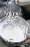 ボウルに入れた生クリームを泡立て器で混ぜている写真