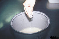 炊飯器に入った研ぎ終えたお米の上に、指先でつまんだ少量の粉ゼラチンをパラパラと振りかけている様子の写真