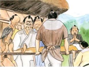 茅葺き屋根の建物の前で、横たわった人物を乗せた担架を運ぶ男性の後ろ姿と、その周りで手を合わせたり悲しげな表情を浮かべたりして見守る村人たちの姿を描いた江戸時代のイラスト